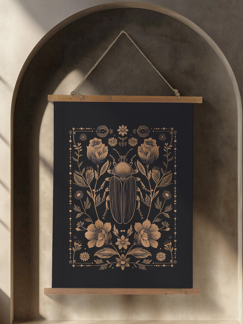 A symmetrical wall tapestry featuring a large scarab beetle in antique bronze tones surrounded by detailed flowers and botanical elements on a black background, mounted on wooden dowels with twine.